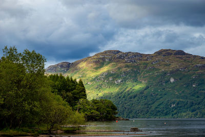 Scenic view of river by mountains against cloudy sky