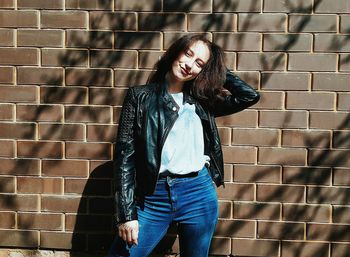 Portrait of smiling woman wearing jacket against brick wall