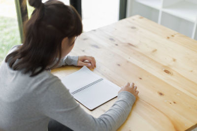 Teenage girl with blank spiral notebook sitting at table