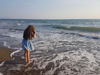 Girl standing in sea against sky