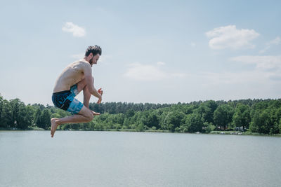 Side view of shirtless man jumping in water against sky