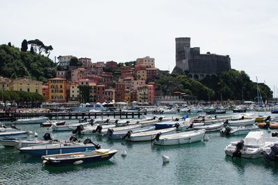 Sailboats moored on sea against buildings in city against sky