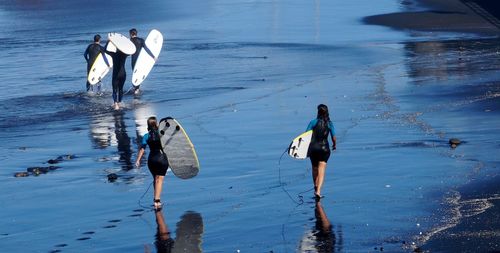 Rear view of surfers carrying surfboard on shore