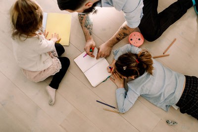 High angle view of father assisting daughters in drawing on floor at home