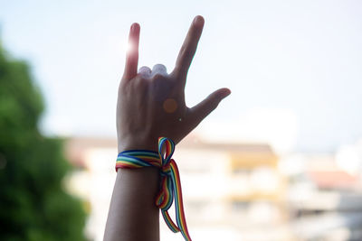 Low angle view of hand wearing rainbow colored wristband gesturing against sky