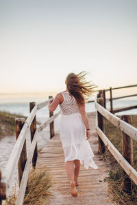 Rear view of woman walking on beach against clear sky