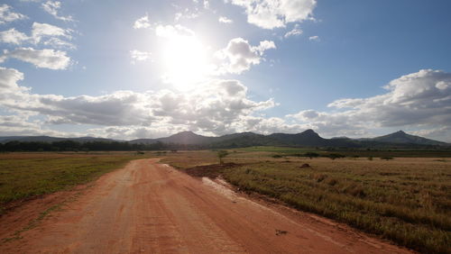 Dirt road amidst field against sky