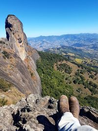 Low section of man standing on rocky mountain against clear sky