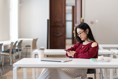 Asian student girl chatting in social media on smartphone while studying in university library