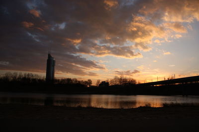 Silhouette buildings against cloudy sky at sunset