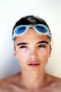 Close-up of boy with swimming goggles against white background