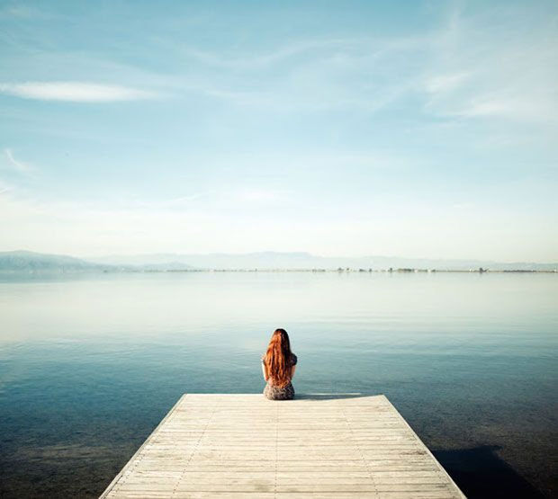 REAR VIEW OF WOMAN SITTING ON PIER AT LAKE