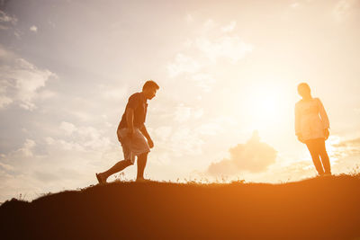 Man and woman walking on field against sky during sunset