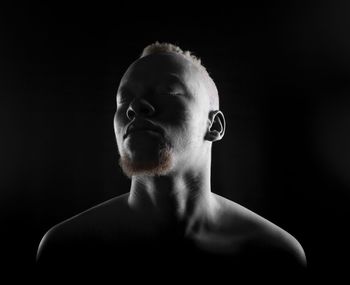 Close-up of shirtless man with eyes closed against black background