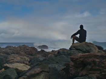 Man standing on rock by sea against sky