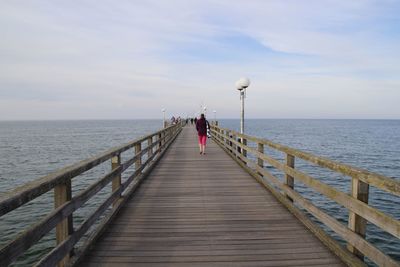 Rear view of man on pier at sea against sky