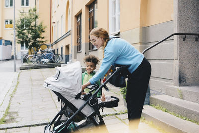 Smiling mother and son looking at baby stroller outside apartment