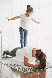Girl standing on mother back exercising at home