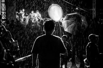 Rear view of boy with balloon standing outdoors during rainy season