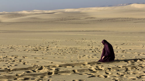 Woman praying on sand in desert