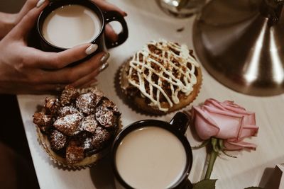 Female hands holding a cup with white coffee, cakes, roses