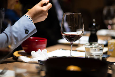 Midsection of person holding wine glass on table in restaurant