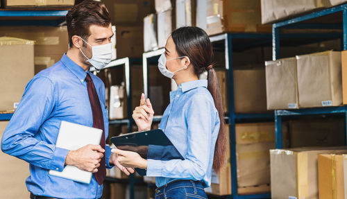 Smiling businesswoman talking with businessman wearing mask in warehouse