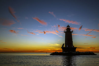 Lighthouse by sea against sky during sunset