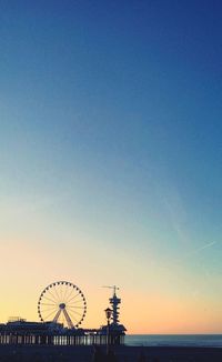 Silhouette ferris wheel against sea at sunset