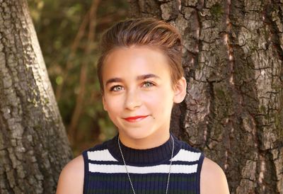 Portrait of smiling girl with short hair against tree trunk