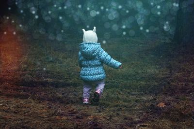 Rear view of baby girl wearing warm clothing walking on field in forest