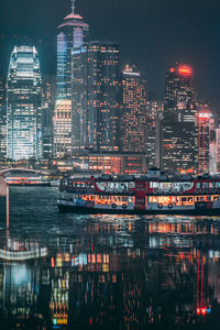 Illuminated modern buildings by river in city at night