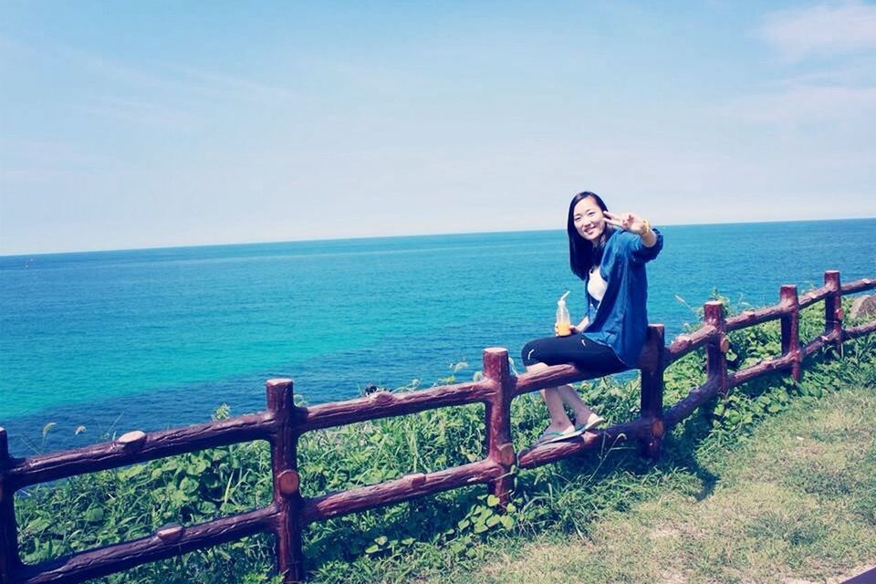 sea, horizon over water, water, sky, railing, lifestyles, leisure activity, beauty in nature, scenics, full length, tranquility, tranquil scene, nature, standing, rear view, casual clothing, blue, sitting