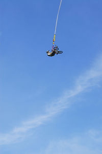 Low angle view of man with bicycle hanging against blue sky