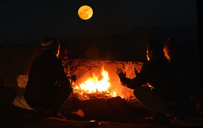 Rear view of men crouching by bonfire at night