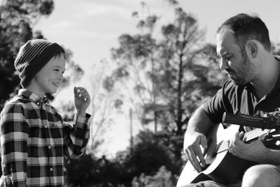 Smiling boy with father playing guitar in park
