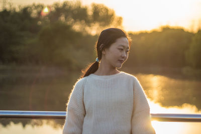 Thoughtful young woman standing against lake during sunset