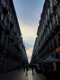 People on street amidst buildings in city against sky