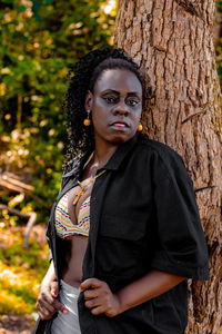 Portrait of young woman standing on tree trunk