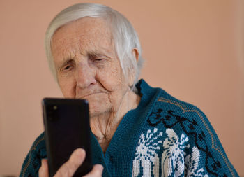 Happy elderly 90-year-old woman wearing a jacet smiles using a smartphone, video call conversation