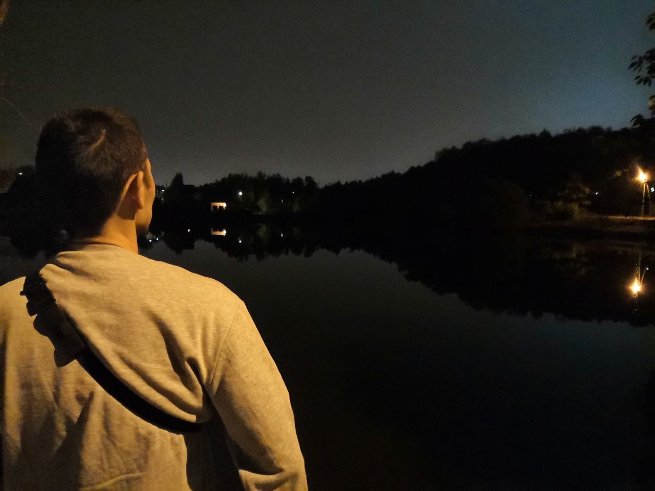 REAR VIEW OF MAN LOOKING AT LAKE AGAINST SKY AT NIGHT