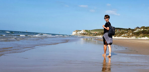 Side view of woman with backpack walking at beach against sky