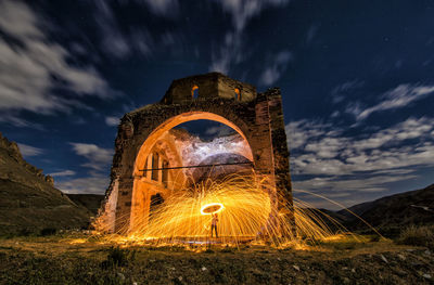 Illuminated lighting equipment on mountain against sky at night