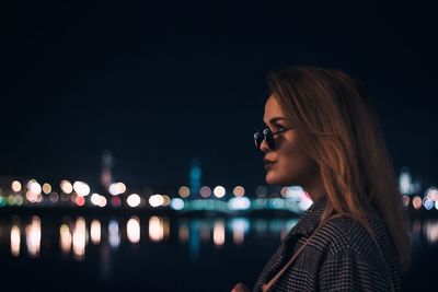 Portrait of young woman looking at illuminated city at night