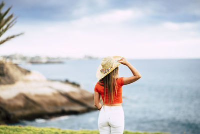 Rear view of woman standing at beach against sky