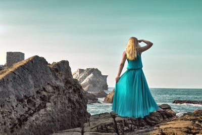 Rear view of woman standing on cliff by sea against sky