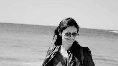 Portrait of smiling young woman standing at beach against clear sky