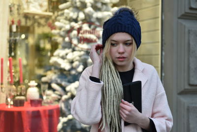 Young woman looking away while standing by retail display of store in winter