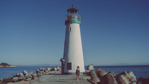 Lighthouse by sea against clear blue sky