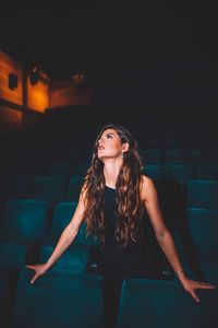 Beautiful young woman looking away while standing in movie theater